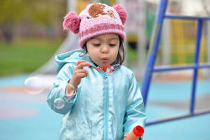 Child in a woolly hat blowing bubbles in the park