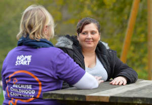 mum and volunteer talking, sitting at a park bench. Volunteer in Home-Start t-shirt with her back to the camera.